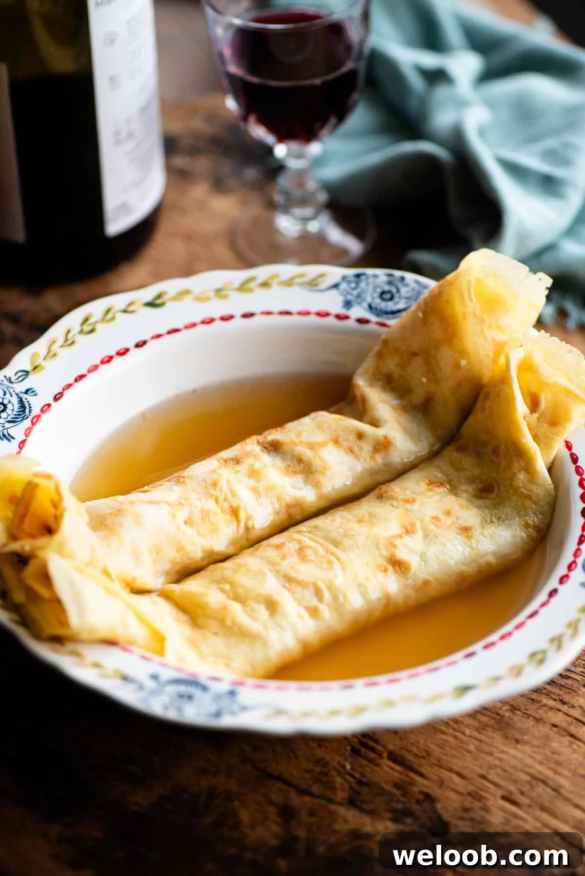 A side shot of Italian crepes in broth in a bowl on a rustic wooden board.