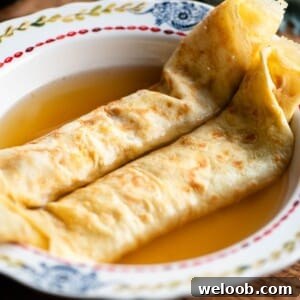 A square cropped image of two crepes in a bowl with broth.