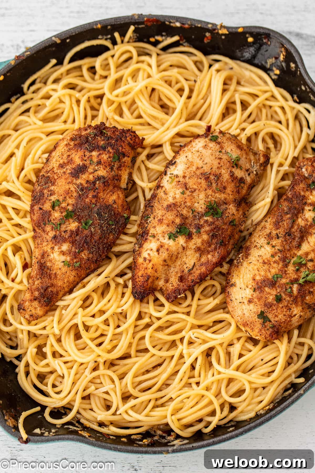 A skillet of garlic butter spaghetti topped with chicken.