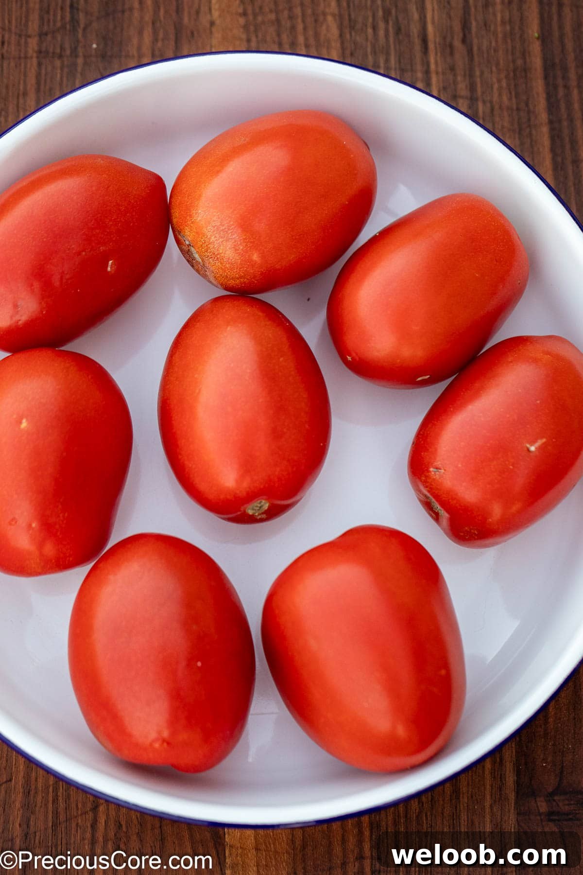 Bright red Roma tomatoes in a white bowl.