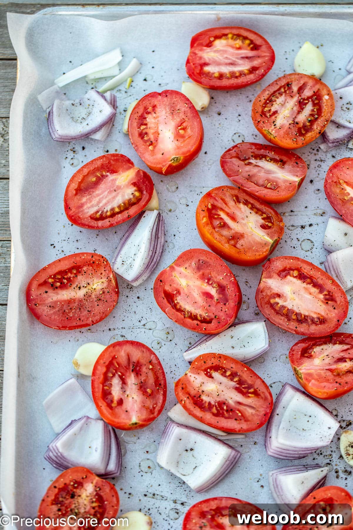Halved Roma tomatoes, onions, and garlic on a sheet pan.