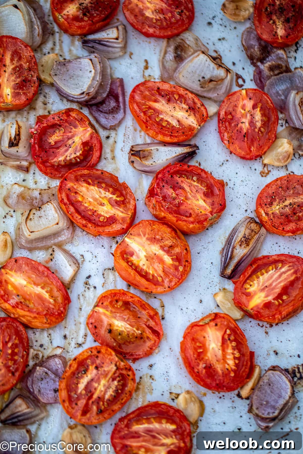 Roasted tomatoes onions and garlic on a sheet pan.