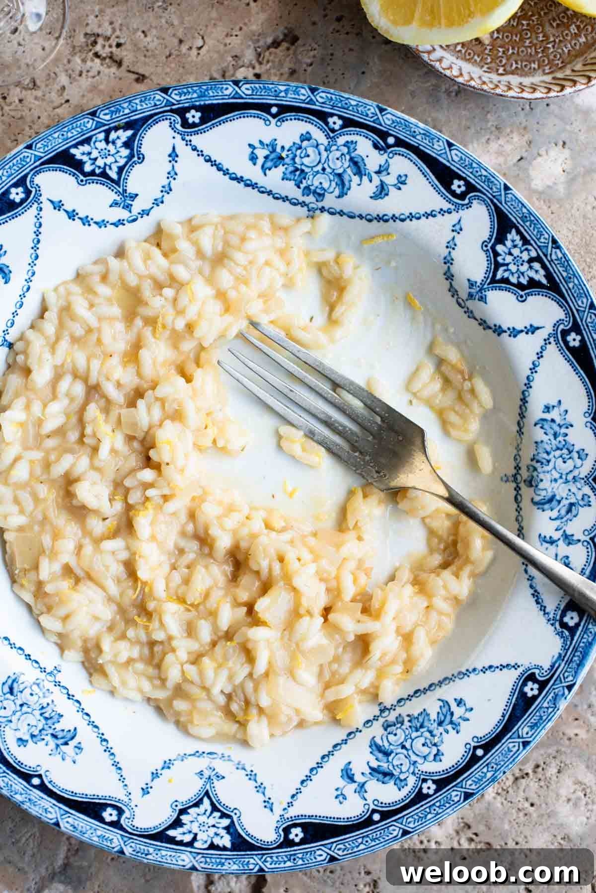 An overhead close up of a bowl of lemon risotto that's half eaten with a fork sitting in the bowl.