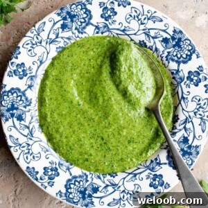 A cropped image of arugula pesto in a blue and white bowl with a spoon.