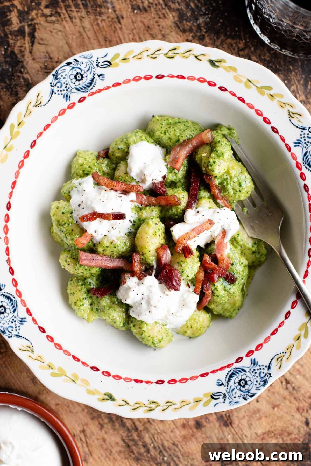 An overhead shot of arugula pesto gnocchi in a bowl topped with crispy pancetta and burrata.