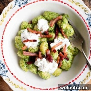 An cropped image of arugula pesto gnocchi in a bowl topped with pancetta and burrata.