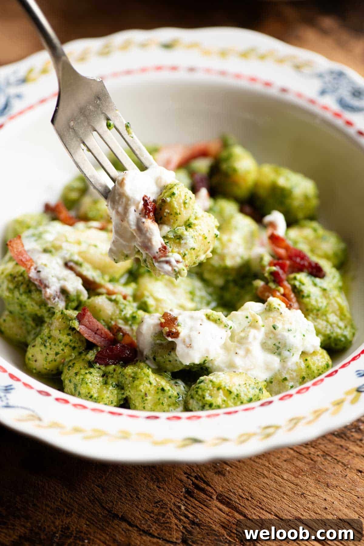 A close up of a fork picking up some arugula pesto gnocchi.