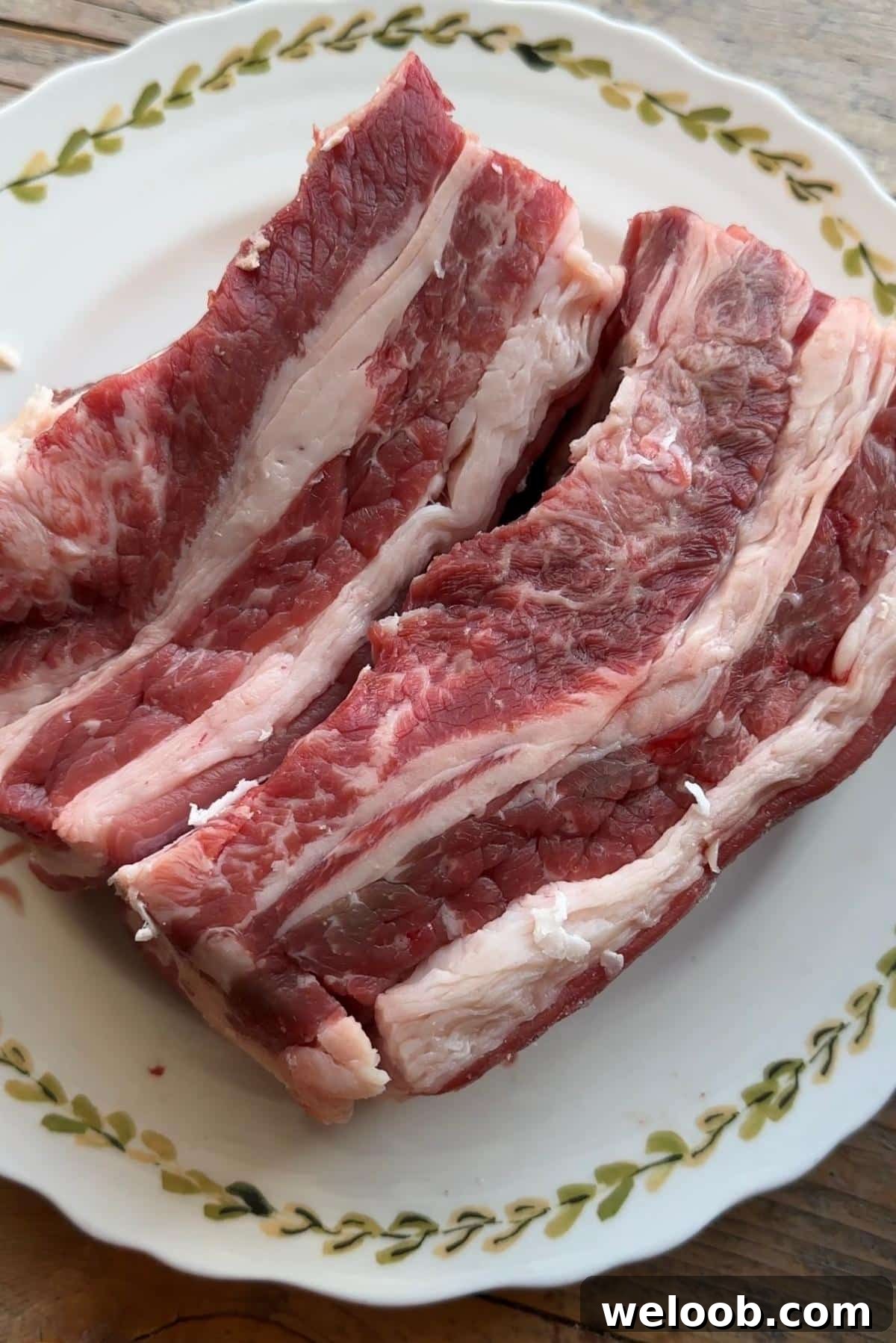 A close up of two beef short ribs on a plate with the lifter muscle attached.