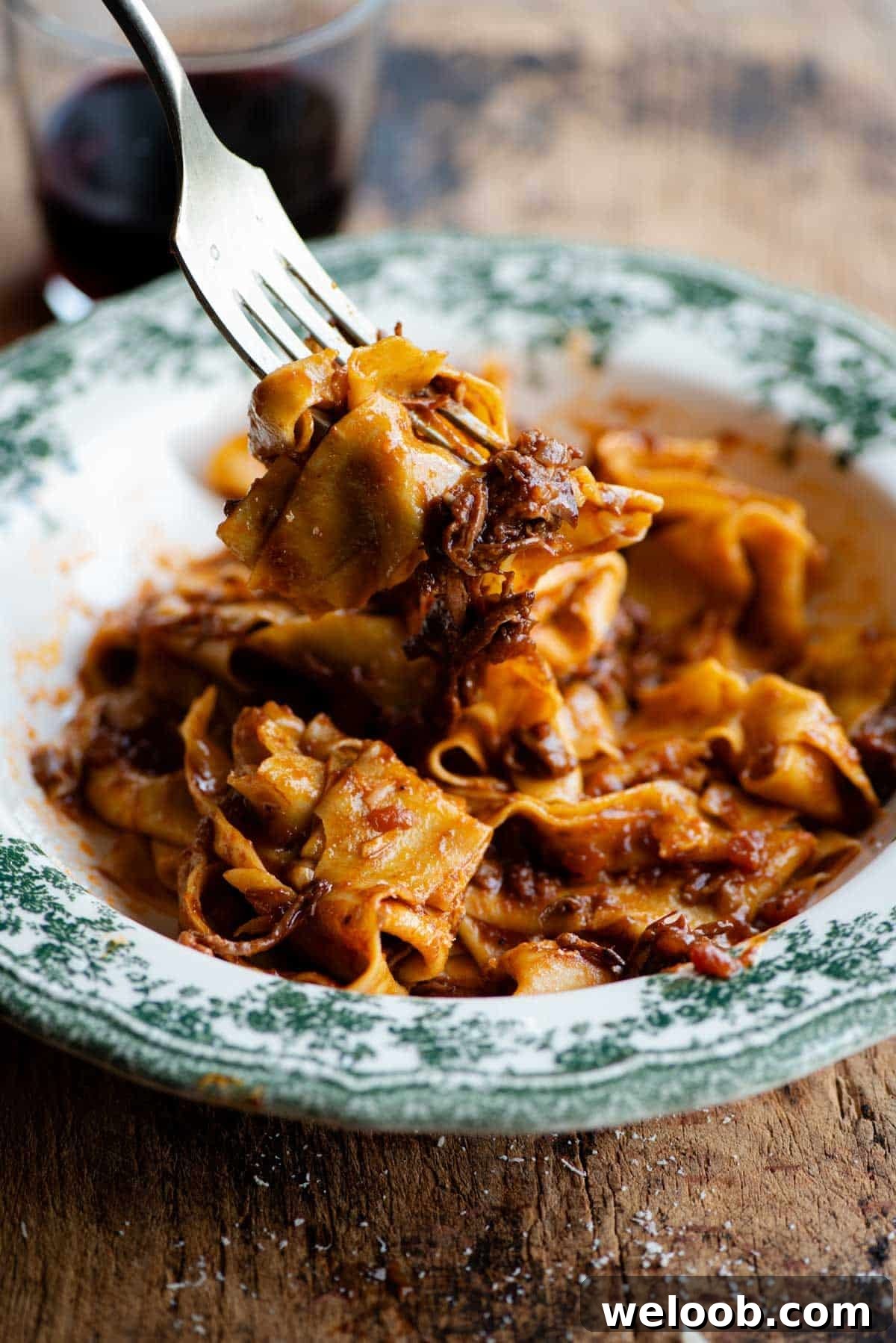 A side shot of a fork picking up some beef ragu and pappardelle pasta.