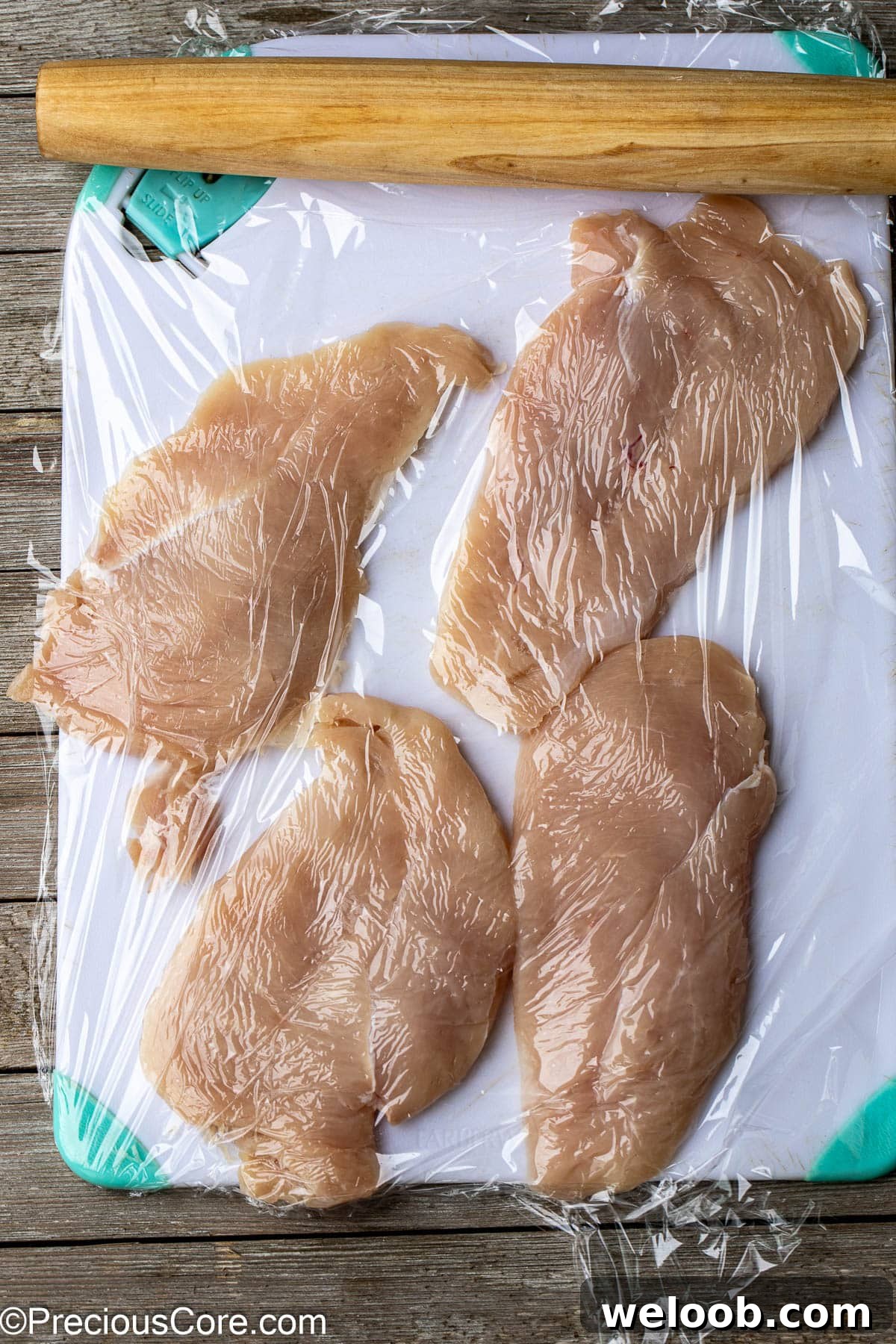 Chicken breasts flatted with rolling pin on chopping board.