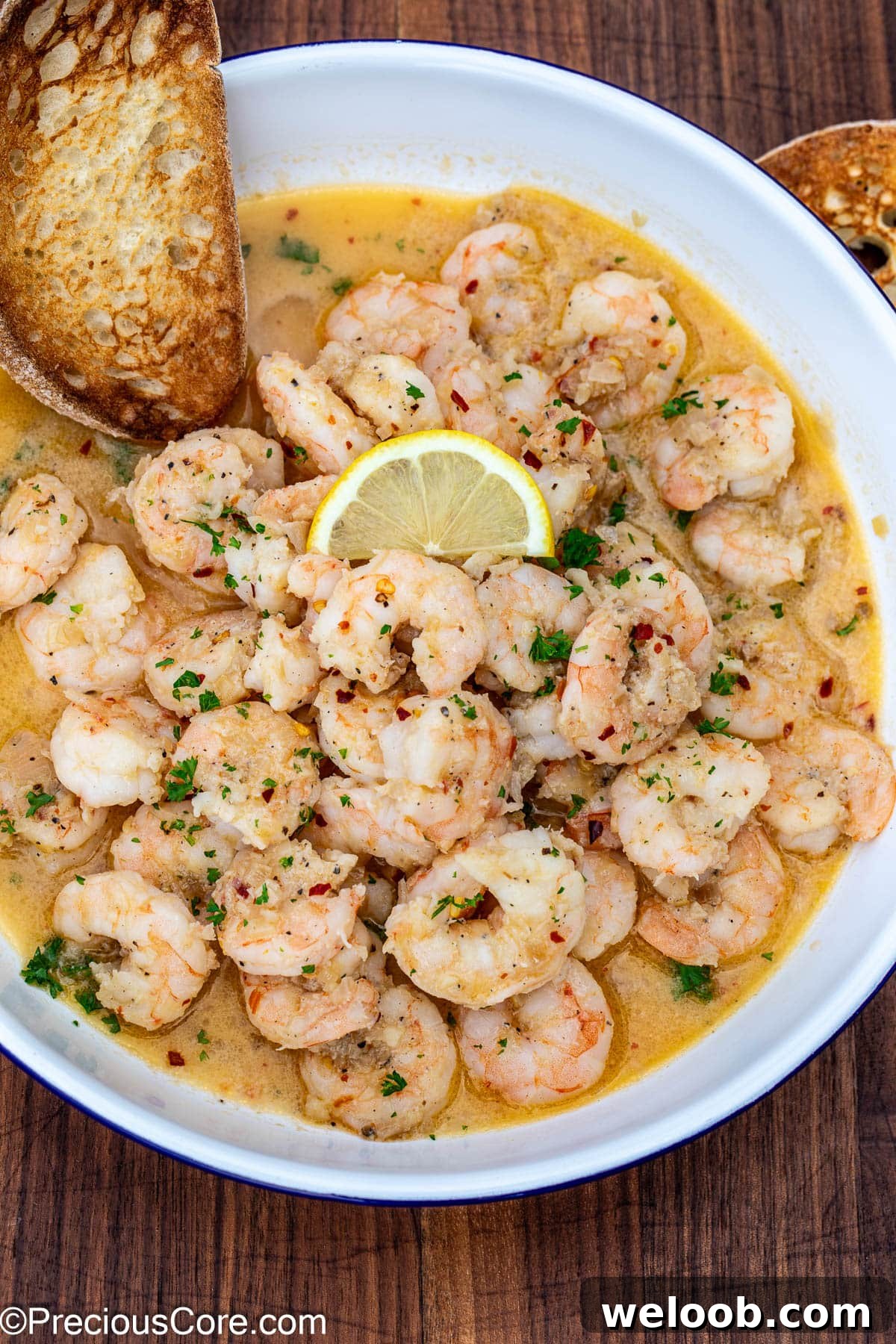 Crusty bread in a bowl of shrimp in white wine sauce.