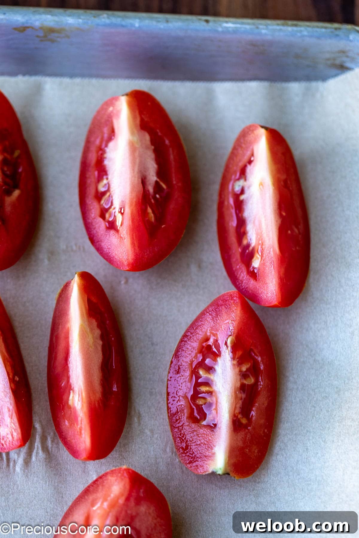 Roma tomatoes cut into quarters on parchment paper.