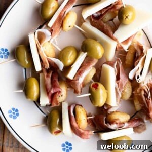 A close up of fried gnocchi on skewers with prosciutto, pecorino and olives.