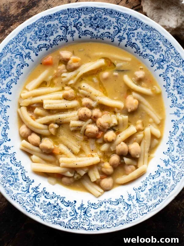 An overhead shot of pasta e ceci (psta and chickpeas) in a blue bowl on a wooden surface.