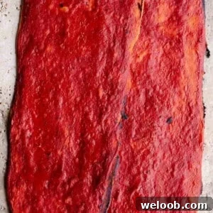 A close up of two long and thin crispy pizzas covered in tomato sauce.
