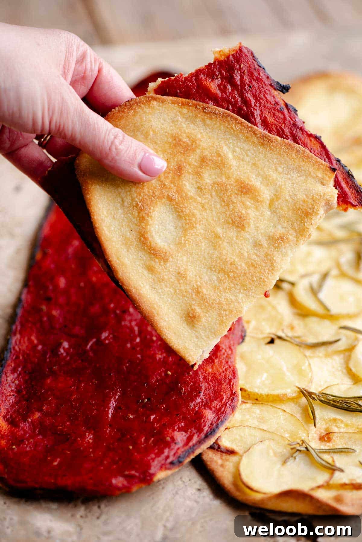 A hand holding a thin and crispy pizza folded in half covered in tomato.