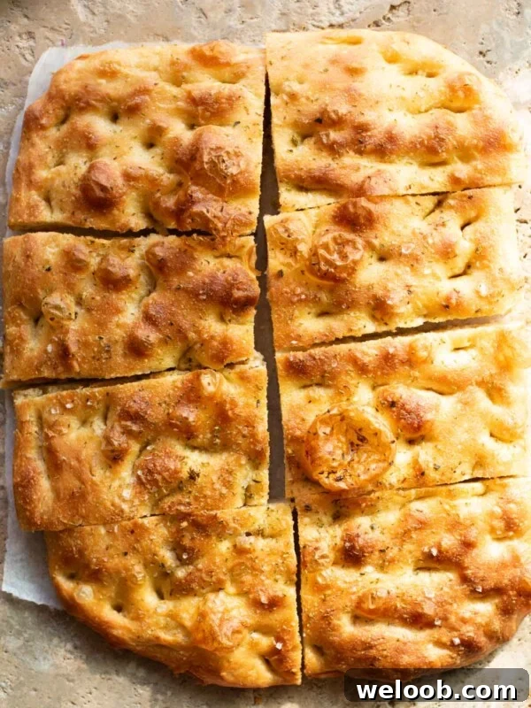 Golden, rustic focaccia bread sliced into rectangular pieces, with a crisp, dimpled crust, a sprinkle of sea salt, and a light seasoning of herbs, resting on a stone surface.