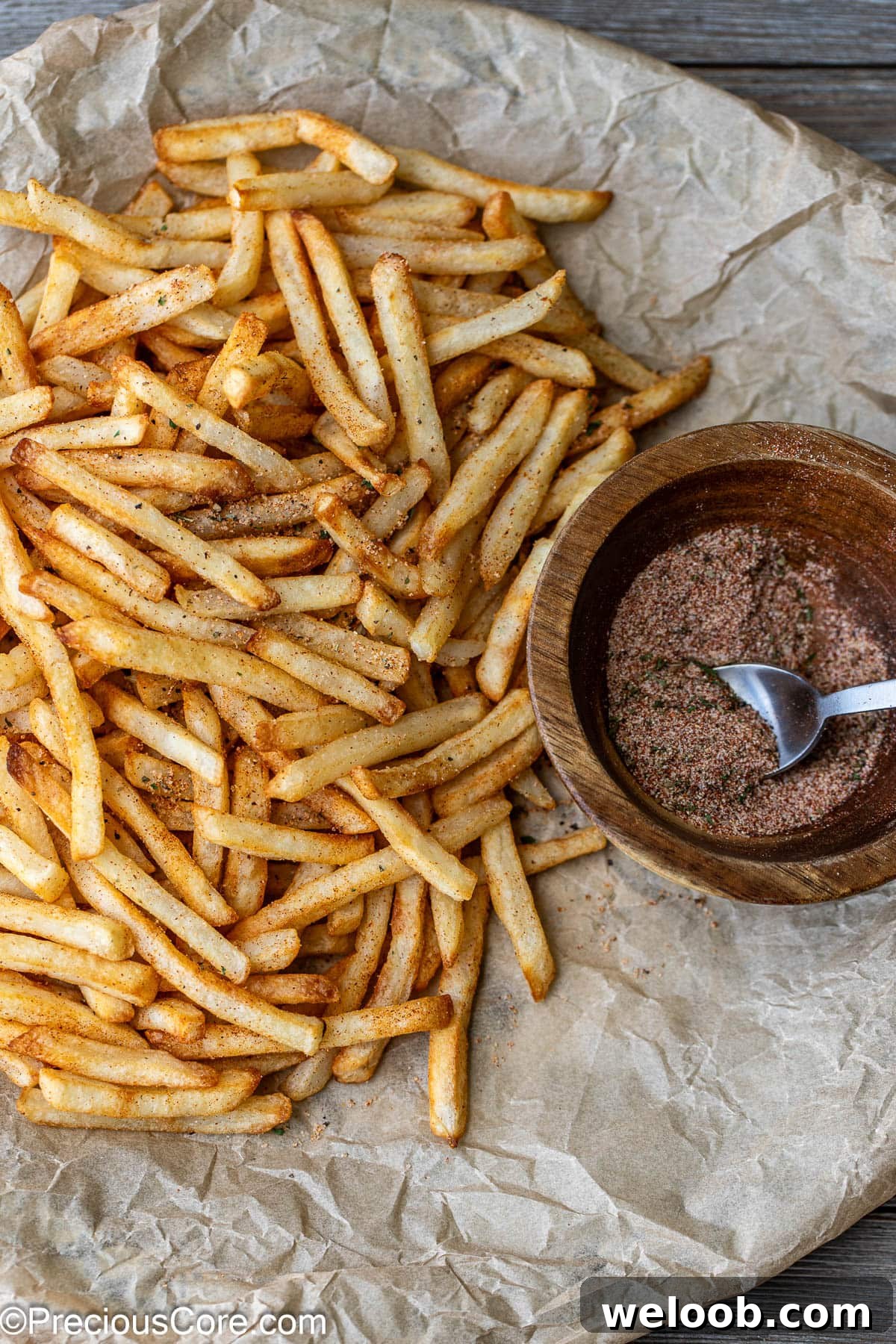 Fries on brown parchment paper with seasoning sprinkled on them.