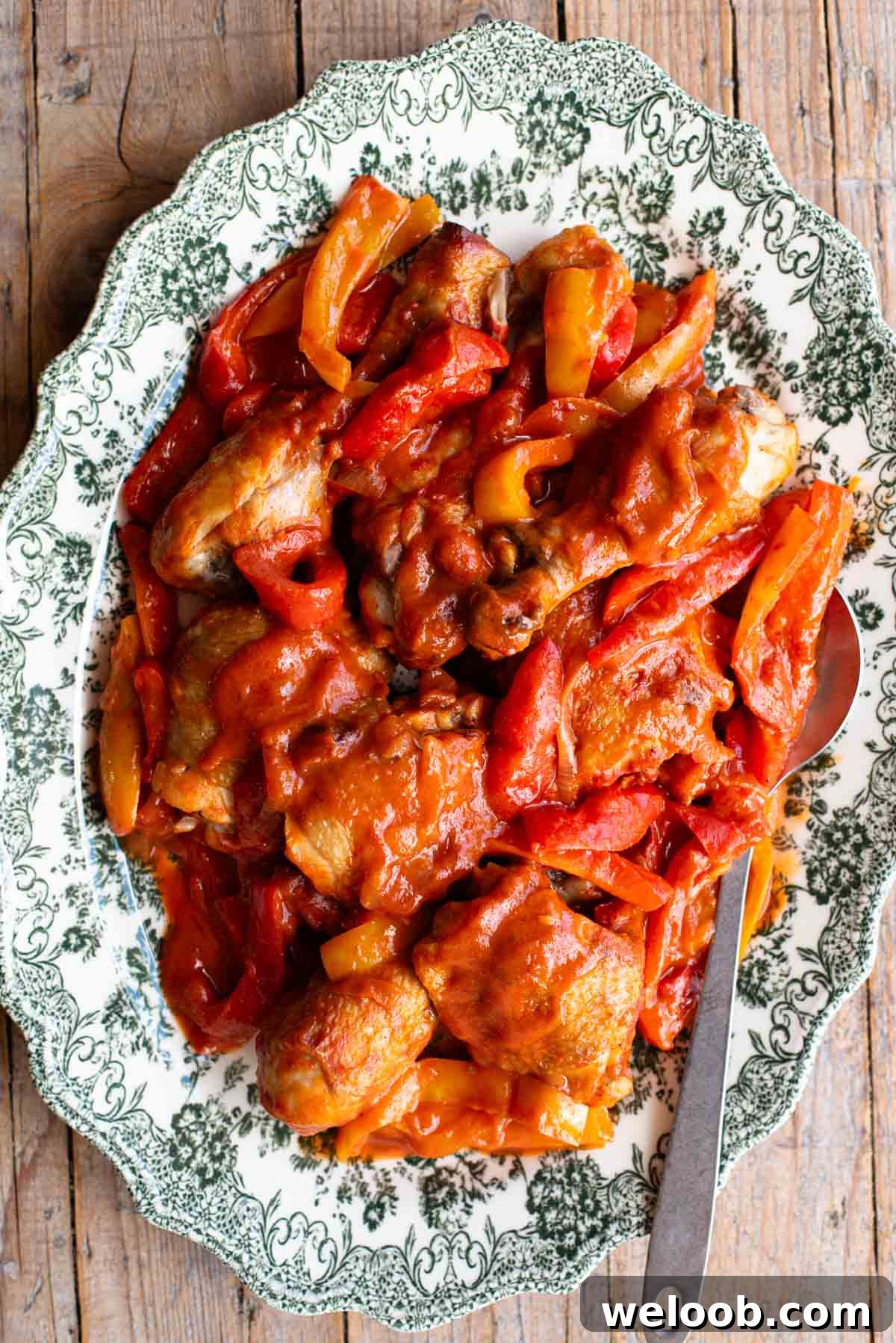 Italian chicken and peppers in a tomato sauce on a large platter serving plate on a rustic wooden surface.