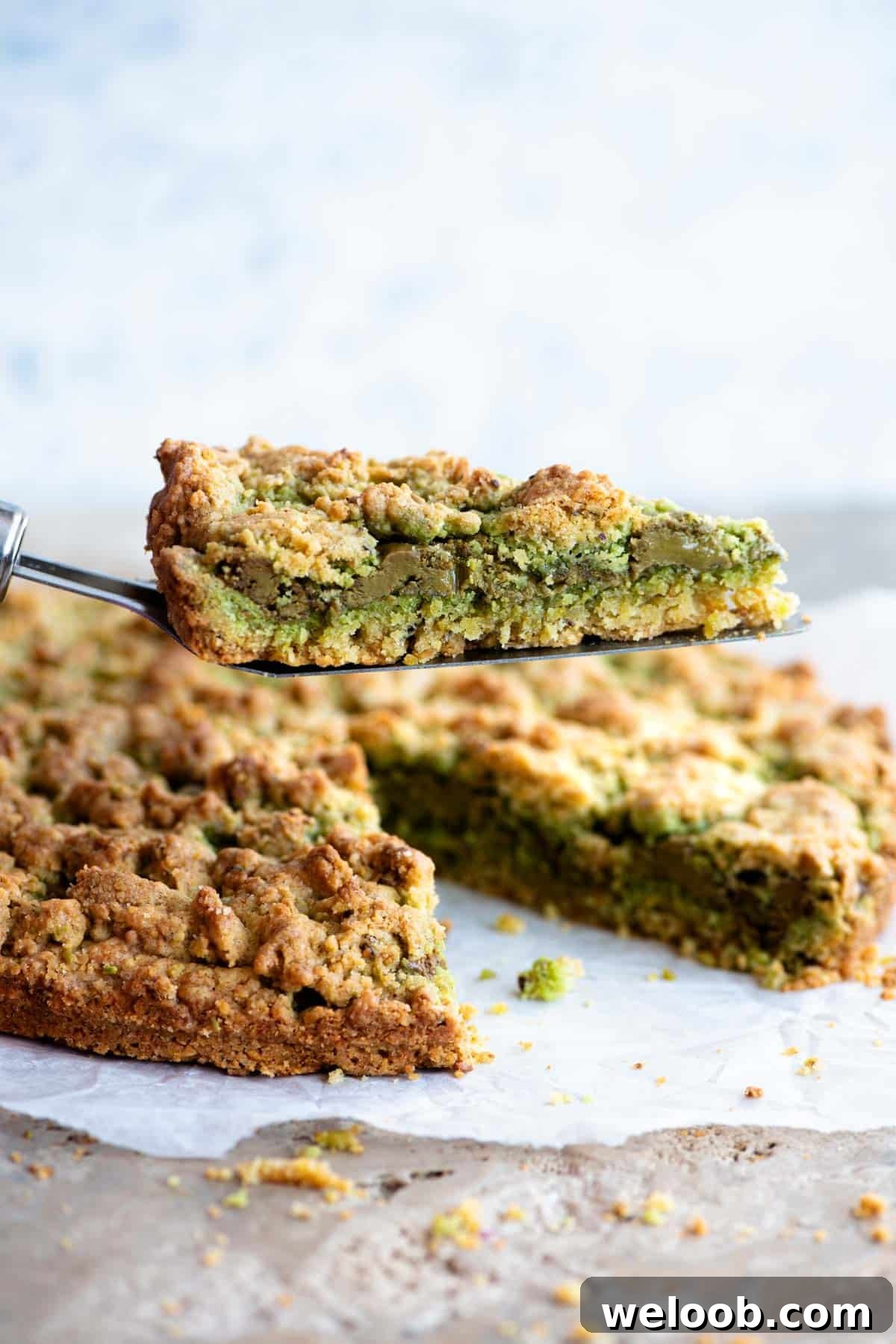A cake slice holding up a slice of pistachio crumb cake showing a layer of pistachio in the middle.