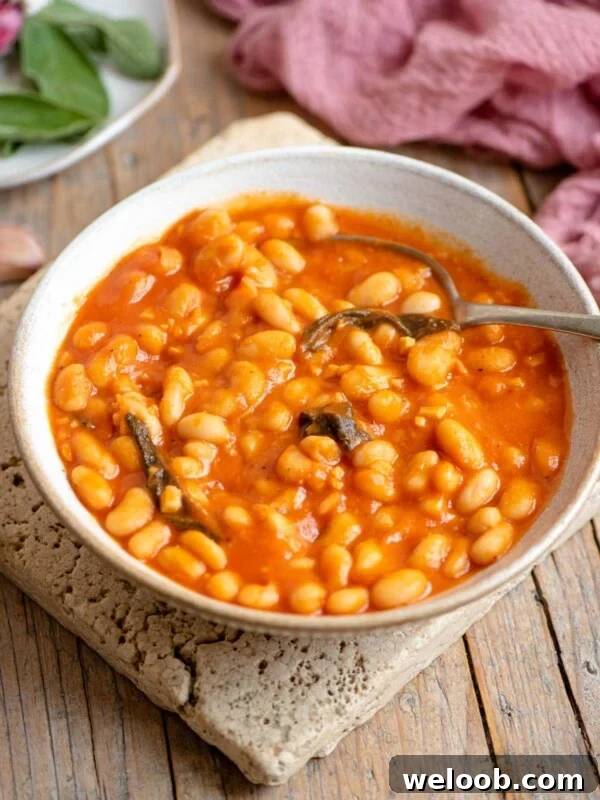 A bowl of cannellini bean in tomato sauce with sage sitting on a wooden surface