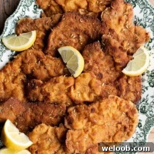 A close up of breaded pork cutlets on a serving plate with lemon wedges.