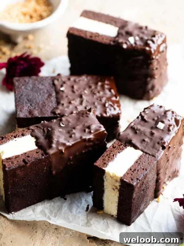Four chocolate ice cream sandwiches with vanilla ice cream in the middle and dipped in chocolate and hazelnuts on a travertine surface.