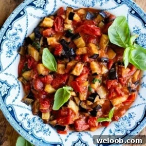 A close up of fried eggplant in a cherry tomato and basil sauce. It's presented in a blue and white country style bowl.