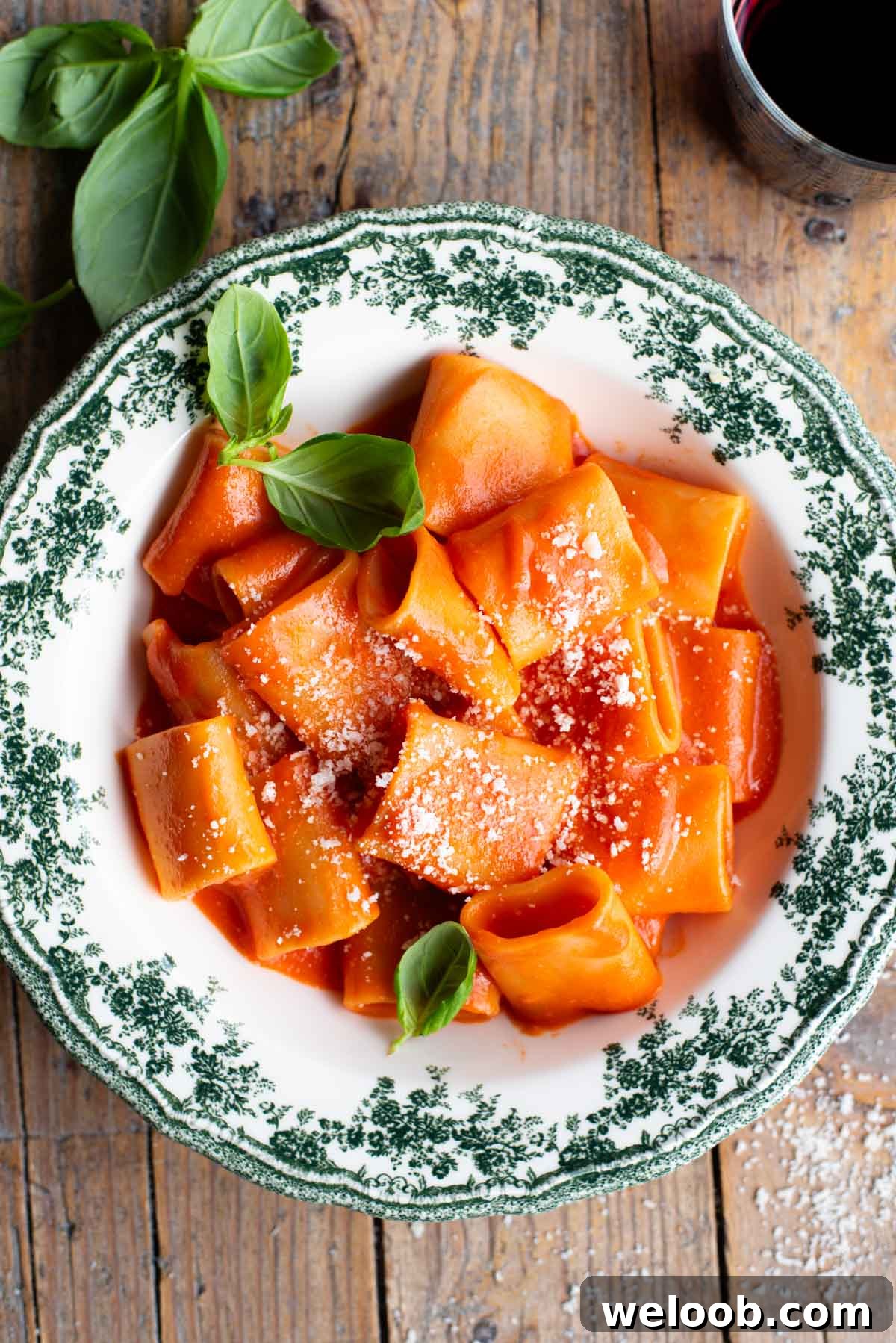 Paccheri pasta with a smooth tomato sauce in a green and white patterned bowl topped with basil.