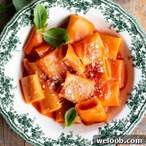 Paccheri pasta in a smooth tomato sauce in a green and white patterned bowl garnished with basil.