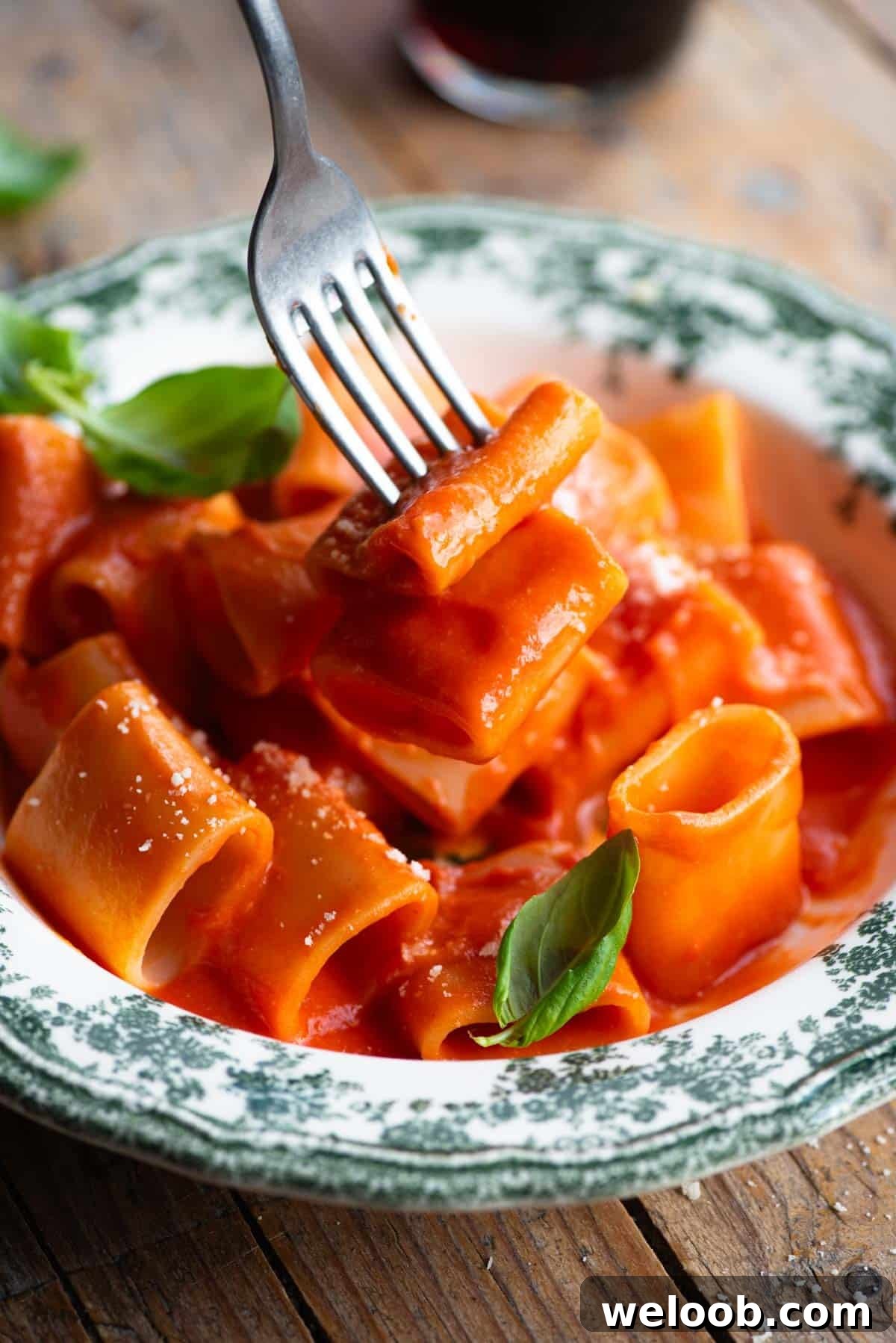 A close up of a fork picking up paccheri pasta with tomato sauce.