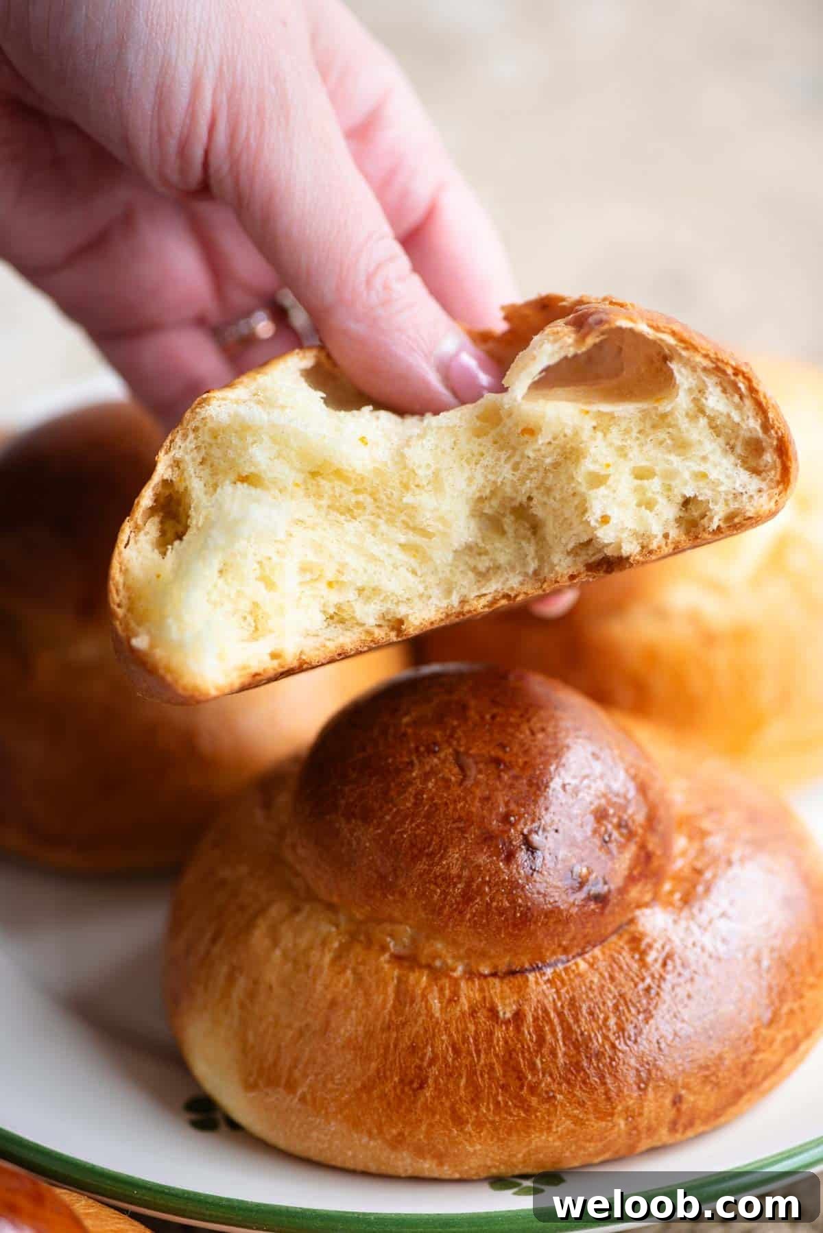 A hand holding a Sicilian brioche bun cut in half showing the airy interior.