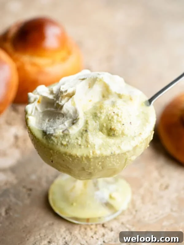 A close up of pistachio granita in a glass serving bowl topped with whipped cream and a brioche bun behind it.
