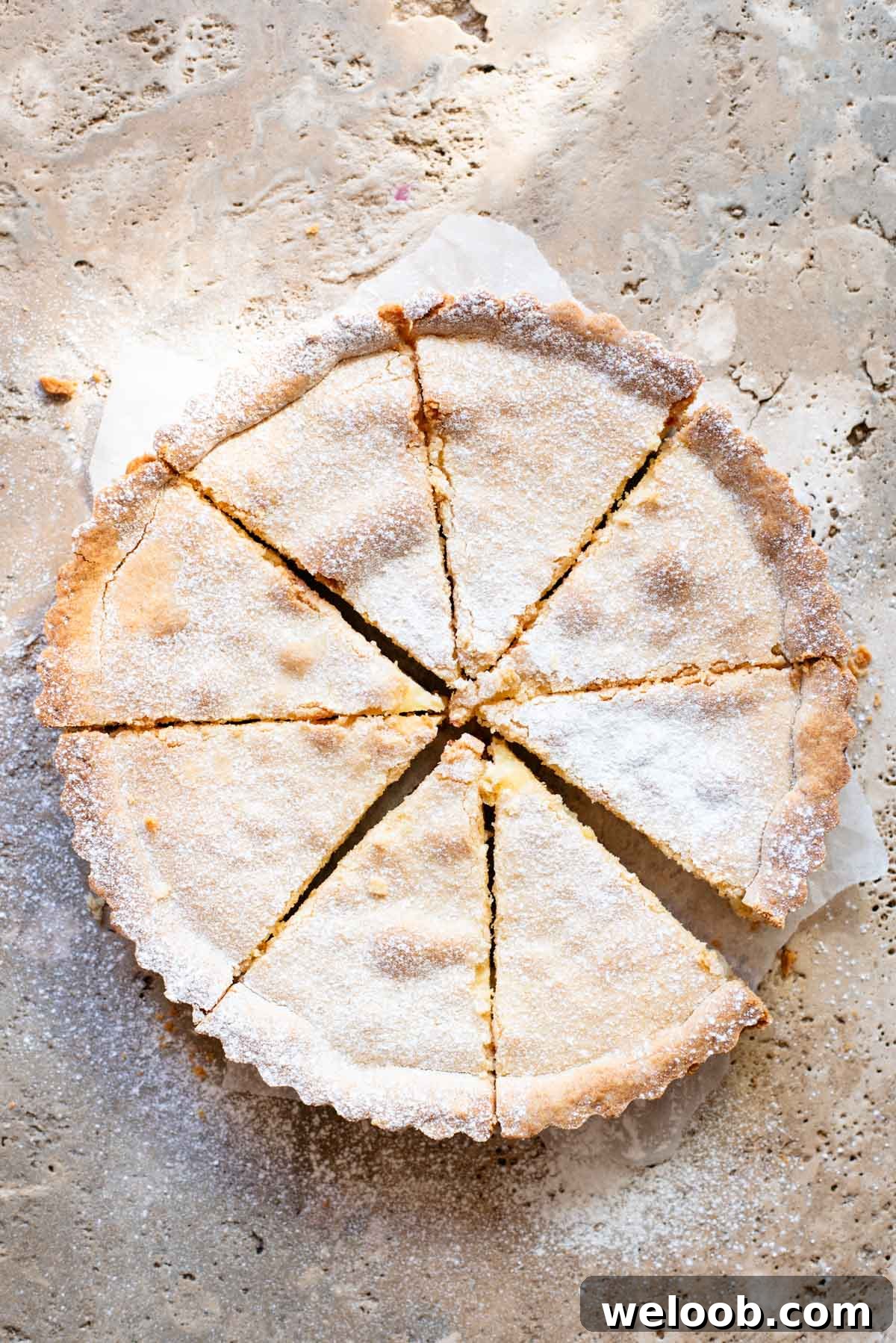A crostata cut into 8 slices and dusted in powdered sugar sitting on a travertine surface.