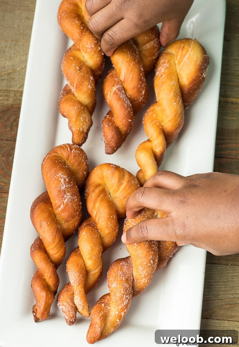 Hand grabbing a twisted African doughnut from a platter of doughnuts.