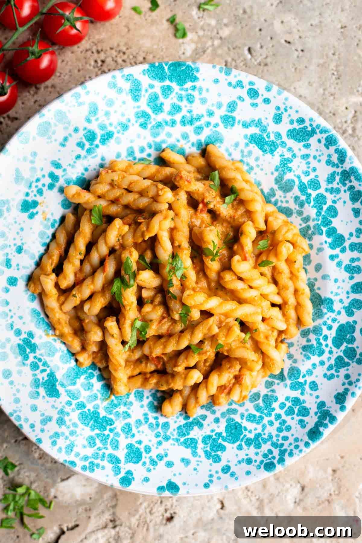 Pasta in a tuna tomato sauce in a blue and white spotted plate sitting on a travertine surface.