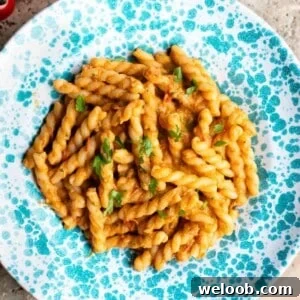 A cropped close up of tuna pasta sauce with gemelli pasta in a blue and white speckled bowl.