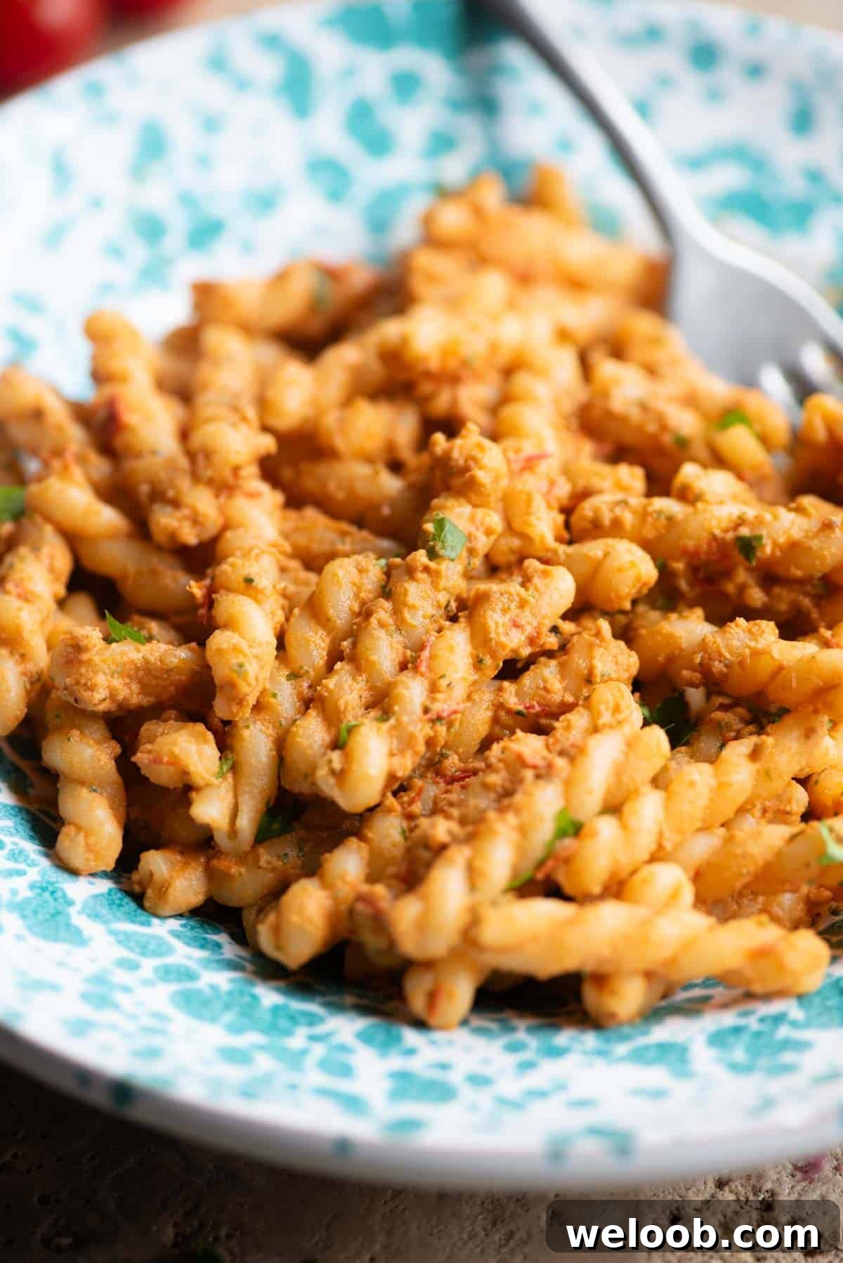A close up of fusilli pasta with a tuna and tomato sauce in a blue and white bowl.