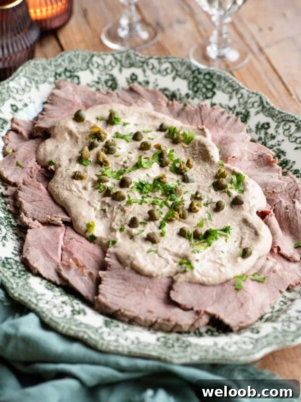 Vitello Tonnato on a serving platter topped with sauce, capers and parsley.