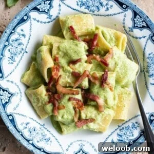 A close up of a creamy zucchini pasta topped with crispy pancetta.