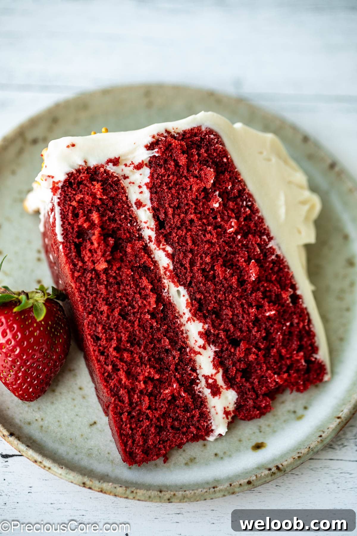 Slice of red velvet cake without buttermilk with strawberry on the side.