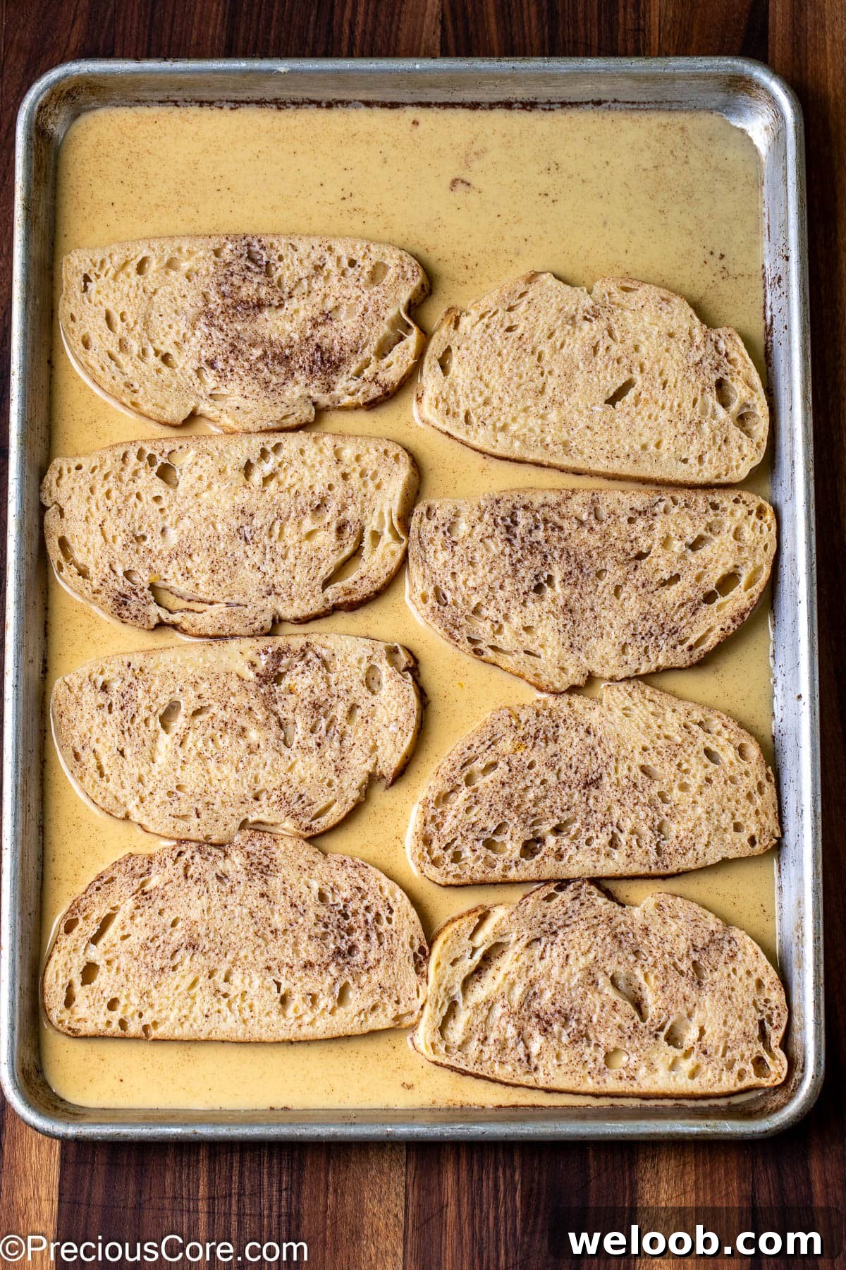 Bread slices soaking in custard on a baking sheet.