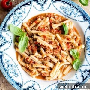 A cropped square image of pasta in tomato sauce in a blue and white vintage style bowl.