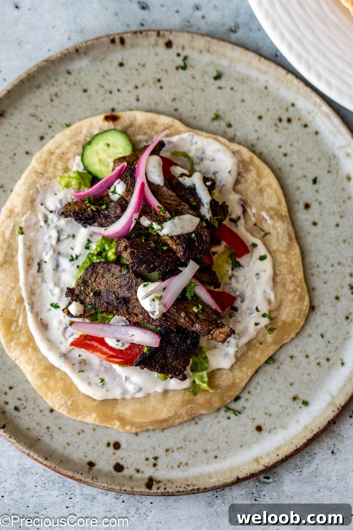 A flatbread topped with beef shawarma, veggies, and sauce.