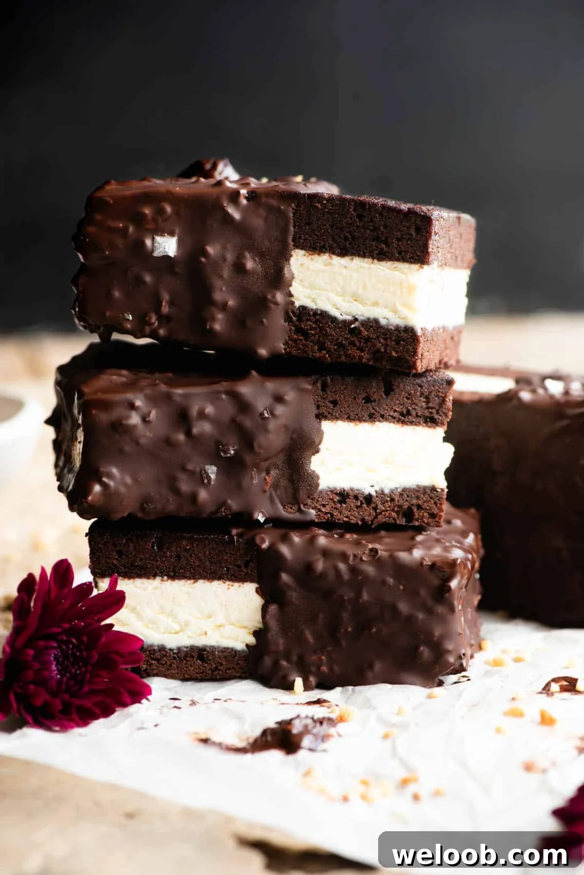 Three chocolate and vanilla ice cream sandwiches stacked on top of each other the surface is travertine and the background is black.