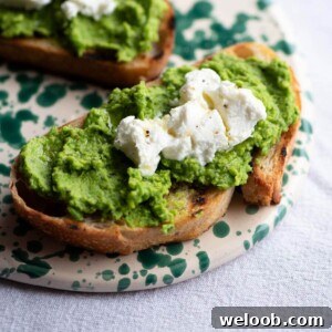 A close up of a slice of bruschetta topped with pea pesto and goats cheese on a ceramic serving board.