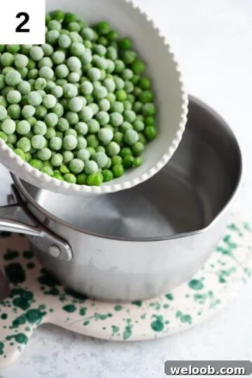 Frozen peas getting added to a small pot of boiling water.