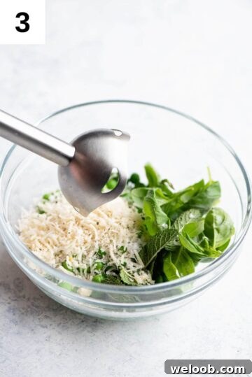 All ingredients for pea pesto in a bowl with an immersion blender over it.