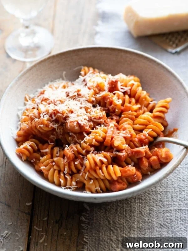 Creamy tomato pasta in a bowl sitting on a wooden surface with a glass of wine in the background