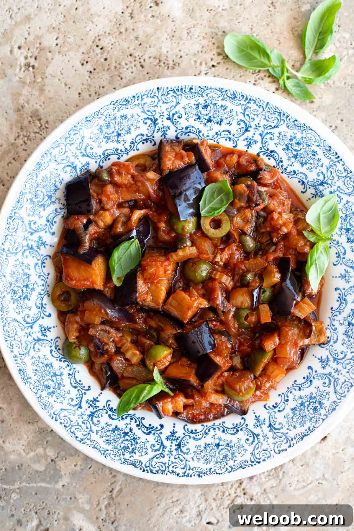 Sicilian caponata in a blue patterned bowl sitting on a travertine surface.